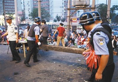 6月13日晚8點，朝陽路和青年路交叉口西側(cè)，一次聯(lián)合執(zhí)法行動中，輔警與協(xié)管抬走商戶的燒烤用具。新京報記者 尹亞飛 攝