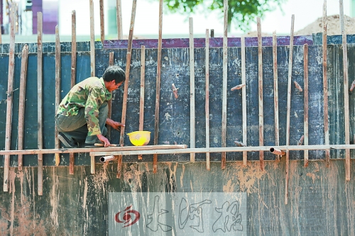　　烈日下，狹窄的架子上，工人正用錘子固定樁基。