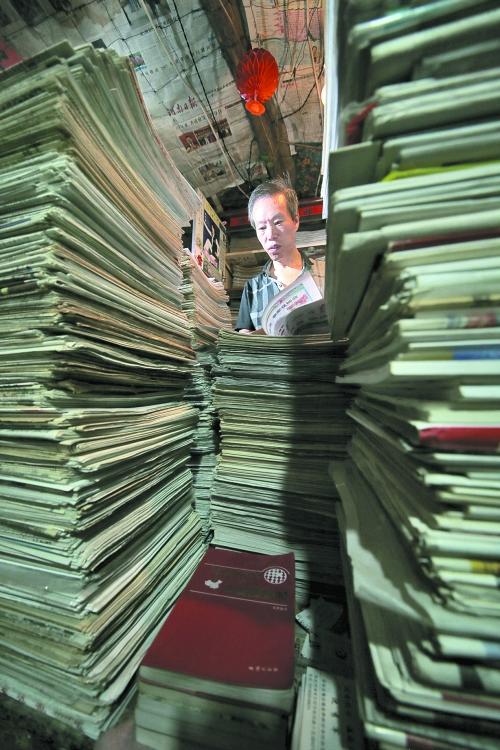 王曉民坐在寫字桌前，被報紙淹沒。