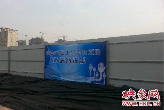 道路南側(cè)圍起了白色的圍擋，墻上標(biāo)示著“因地鐵施工帶來(lái)的不便敬請(qǐng)您諒解”的提示牌。