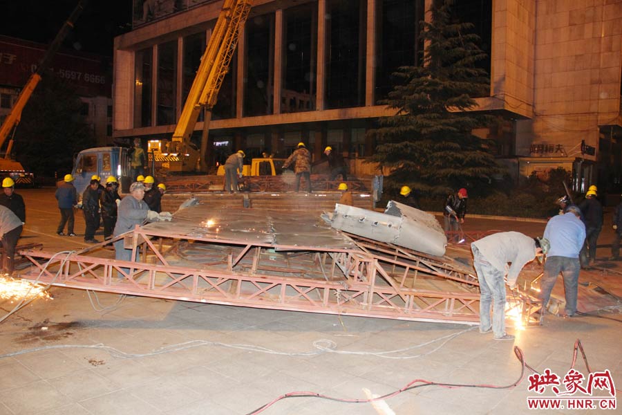 地面上的20多名工人對吊裝下的廣告牌進行分割。