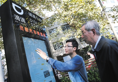 10月15日，滴滴工作人員（左）指導乘客使用“滴滴車站”的電子屏預約出租車。