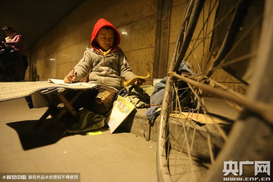 2015年11月8日晚，鄭州，7歲男孩涵洞橋下陪父母練攤，路邊燈下坐小馬扎上寫作業(yè)。