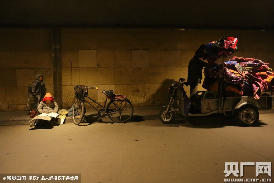 2015年11月8日晚，鄭州，7歲男孩涵洞橋下陪父母練攤，路邊燈下坐小馬扎上寫作業(yè)。