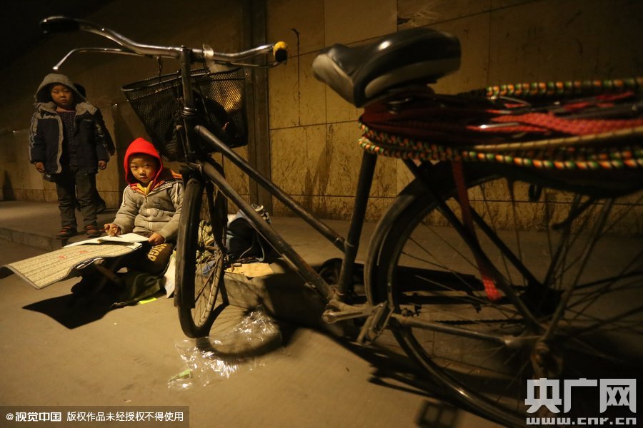 2015年11月8日晚，鄭州，7歲男孩涵洞橋下陪父母練攤，路邊燈下坐小馬扎上寫作業(yè)。