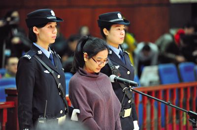 被告人盧梅低著頭，站在朝陽法院刑事審判庭的被告席上。